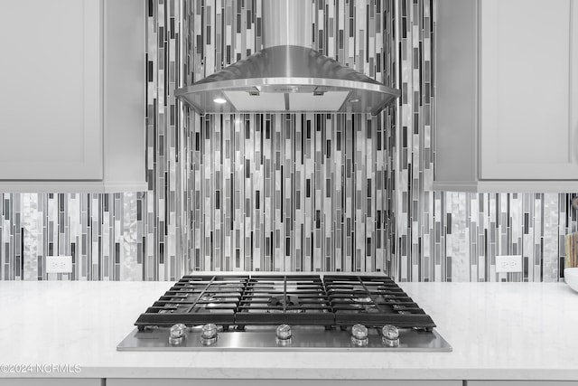 room details featuring decorative backsplash, black gas stovetop, white cabinetry, and island exhaust hood