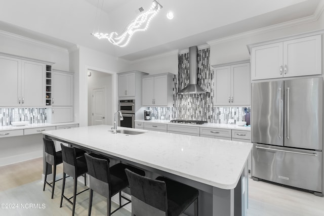 kitchen featuring a kitchen island with sink, wall chimney range hood, sink, decorative backsplash, and appliances with stainless steel finishes