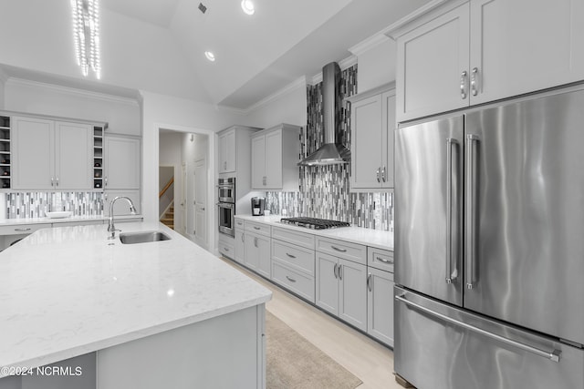 kitchen with appliances with stainless steel finishes, wall chimney exhaust hood, vaulted ceiling, sink, and a center island with sink