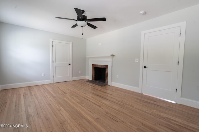 unfurnished living room featuring ceiling fan, a brick fireplace, and light wood-type flooring