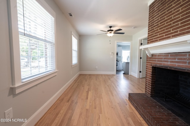 unfurnished living room with brick wall, a fireplace, light wood-type flooring, and ceiling fan