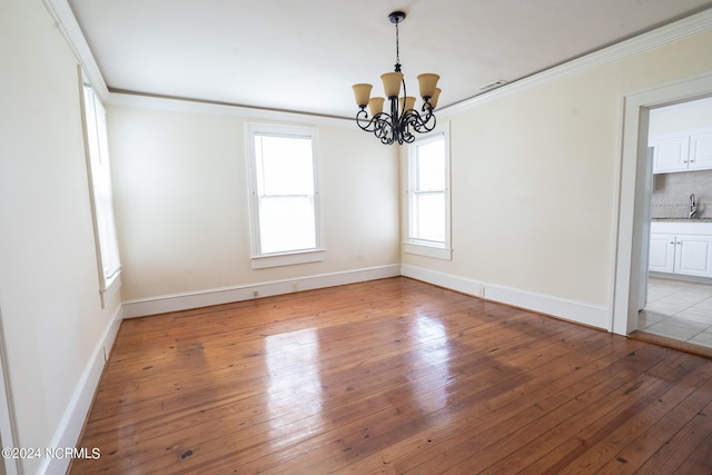 unfurnished dining area featuring crown molding, a chandelier, sink, and light hardwood / wood-style flooring