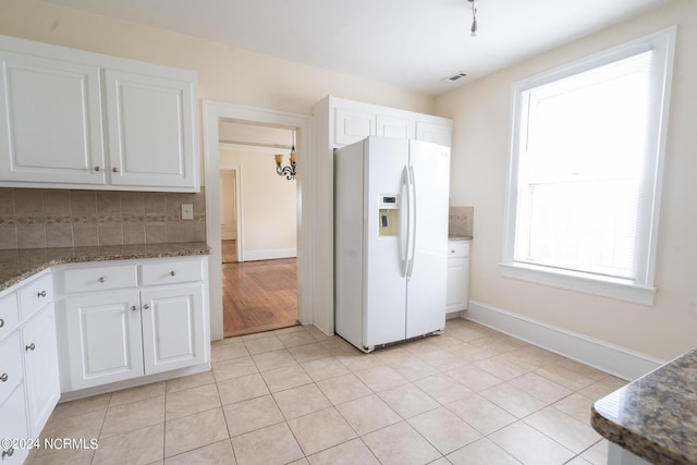 kitchen featuring dark stone countertops, white cabinets, backsplash, white refrigerator with ice dispenser, and light tile patterned floors