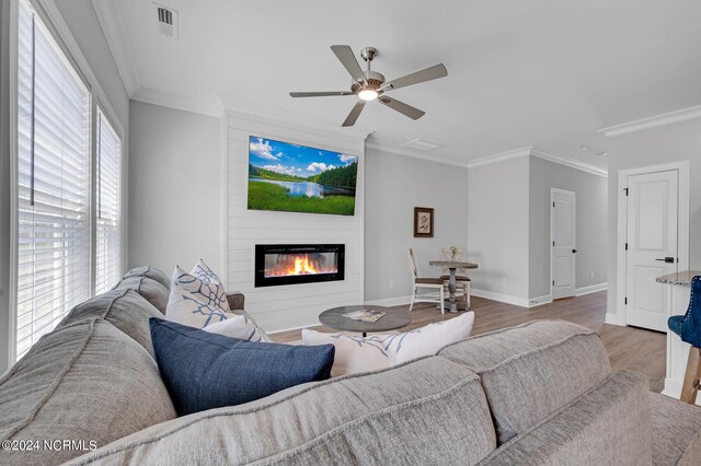 living area with baseboards, ornamental molding, ceiling fan, wood finished floors, and a large fireplace