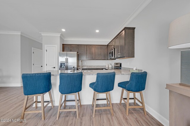 kitchen with dark brown cabinetry, light wood-type flooring, a peninsula, crown molding, and stainless steel appliances