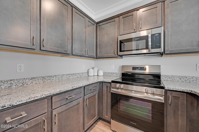 kitchen featuring stainless steel appliances, ornamental molding, dark brown cabinets, and light stone counters