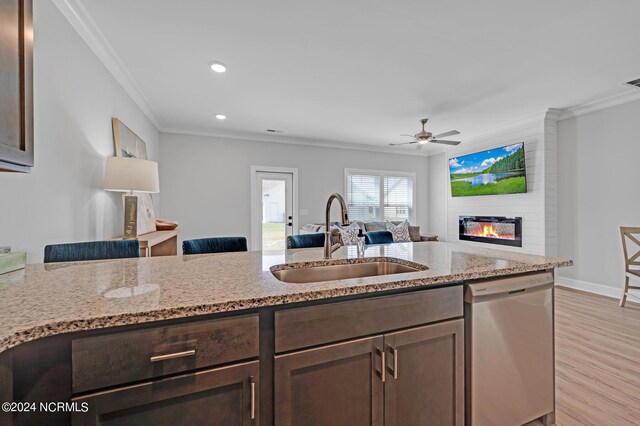 kitchen featuring dishwasher, a sink, ornamental molding, dark brown cabinets, and a large fireplace