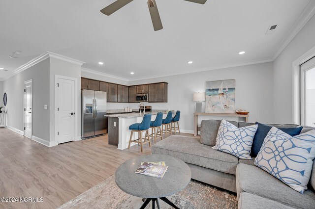 living area featuring baseboards, light wood-type flooring, a ceiling fan, crown molding, and recessed lighting