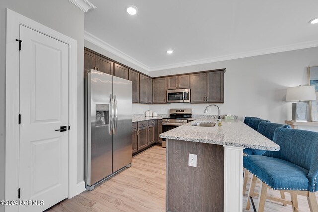 kitchen featuring a breakfast bar, ornamental molding, a peninsula, stainless steel appliances, and a sink