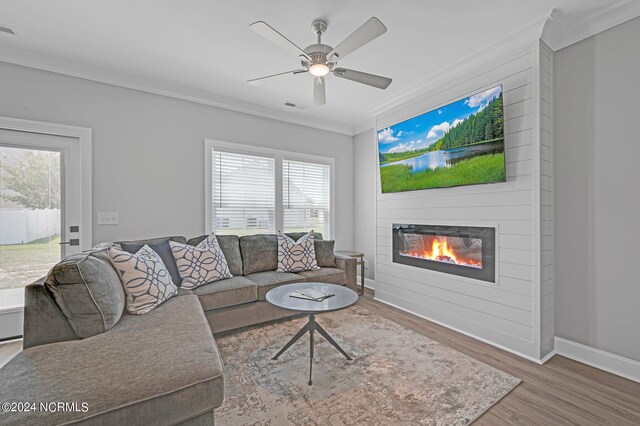 living room with visible vents, ceiling fan, crown molding, wood finished floors, and a glass covered fireplace