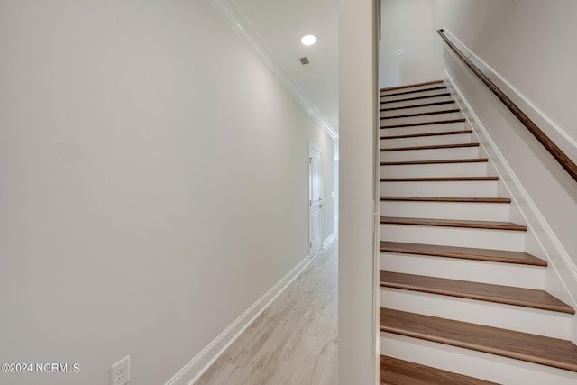 staircase with wood-type flooring and ornamental molding