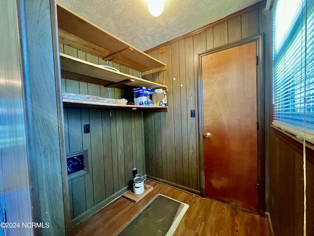 interior space with wooden walls, a textured ceiling, and wood finished floors