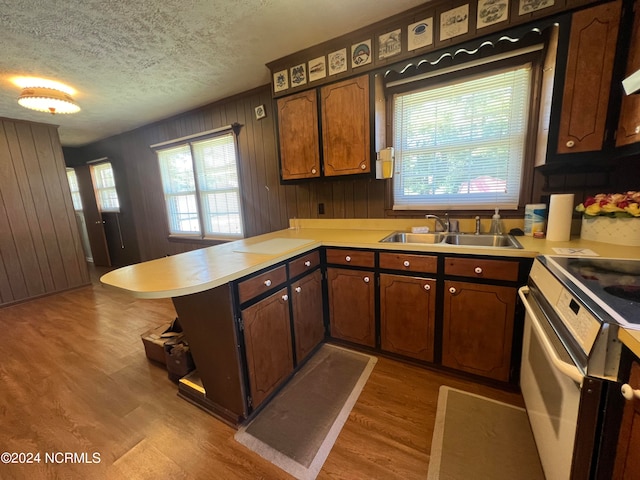 kitchen featuring hardwood / wood-style flooring, sink, kitchen peninsula, wood walls, and a textured ceiling