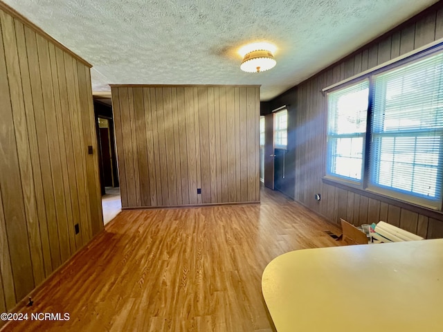 unfurnished room with a textured ceiling, light wood finished floors, crown molding, and wooden walls