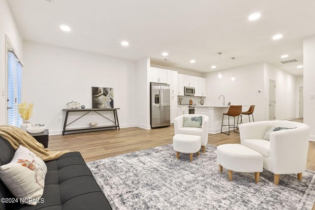 kitchen featuring decorative light fixtures, a kitchen island with sink, stainless steel fridge with ice dispenser, and white cabinetry