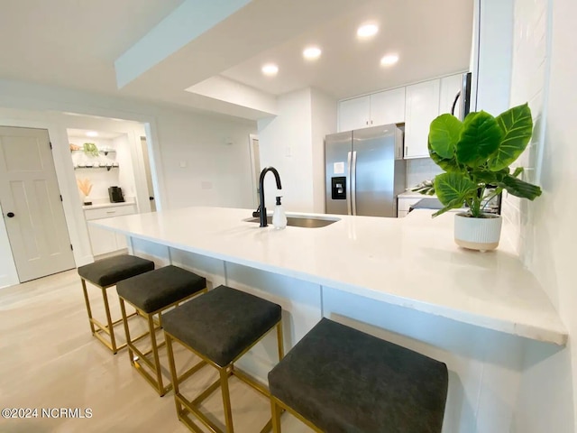 kitchen with sink, stainless steel fridge with ice dispenser, white cabinetry, a kitchen bar, and kitchen peninsula