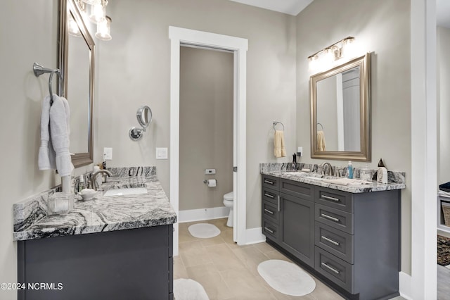 bathroom with baseboards, two vanities, a sink, and toilet