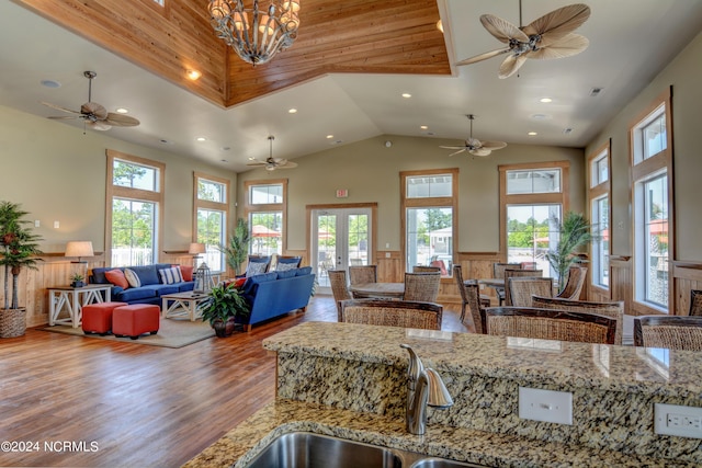 kitchen featuring a wainscoted wall, open floor plan, a healthy amount of sunlight, wood finished floors, and high vaulted ceiling