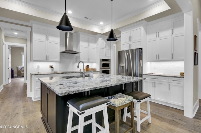 kitchen with wall chimney exhaust hood, white cabinetry, visible vents, and light wood-style floors