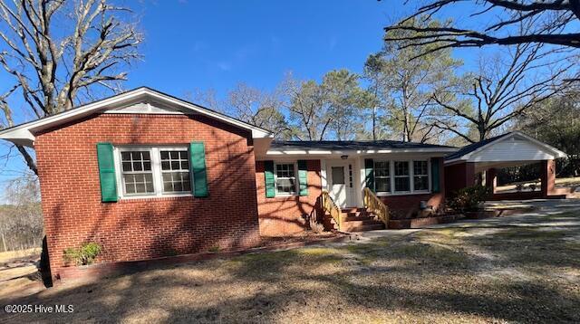 ranch-style home with entry steps, a front lawn, a carport, and brick siding