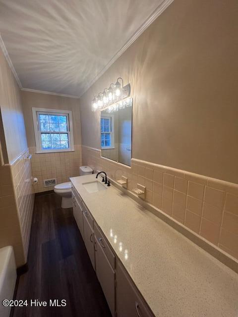 bathroom featuring toilet, hardwood / wood-style flooring, vanity, tile walls, and ornamental molding