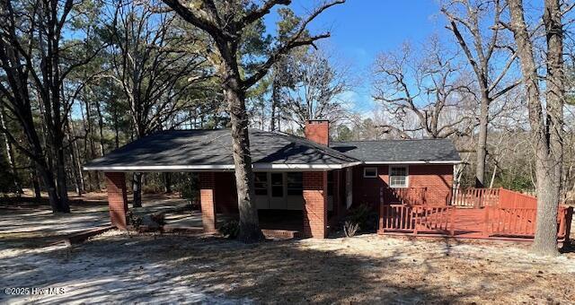 view of property exterior featuring brick siding, a chimney, and a wooden deck