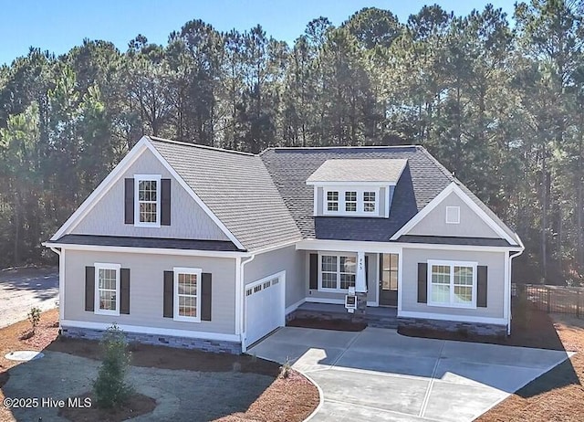 view of front of house with concrete driveway, a forest view, an attached garage, and roof with shingles