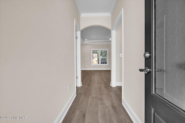 corridor featuring baseboards, arched walkways, crown molding, and wood finished floors