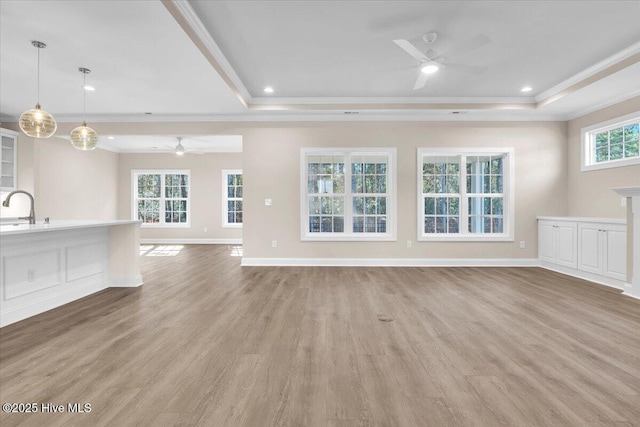 unfurnished living room with light wood finished floors, crown molding, a raised ceiling, and a sink