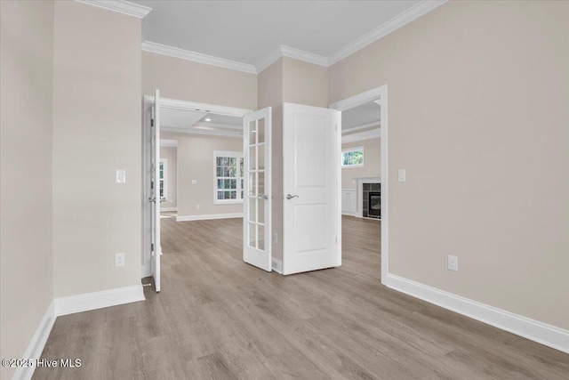 spare room featuring a fireplace with flush hearth, ornamental molding, wood finished floors, and baseboards