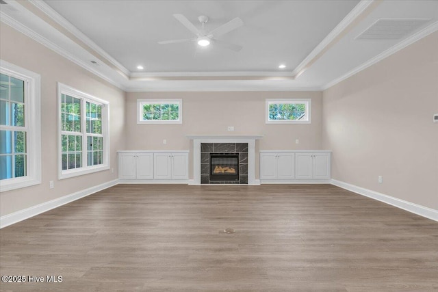 unfurnished living room featuring ornamental molding, a tray ceiling, wood finished floors, and a premium fireplace