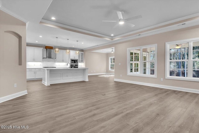 unfurnished living room with light wood-style floors, baseboards, a tray ceiling, and crown molding