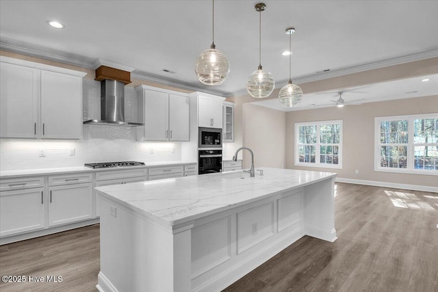 kitchen featuring wood finished floors, stainless steel appliances, crown molding, wall chimney range hood, and a sink