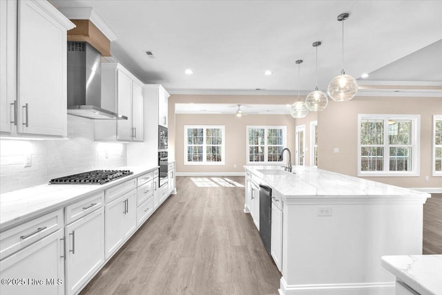 kitchen with stainless steel appliances, a sink, light wood-type flooring, wall chimney exhaust hood, and tasteful backsplash