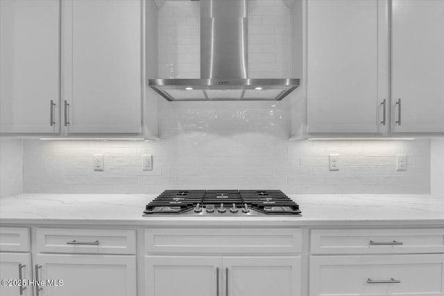 kitchen featuring tasteful backsplash, white cabinets, stainless steel gas cooktop, and wall chimney range hood