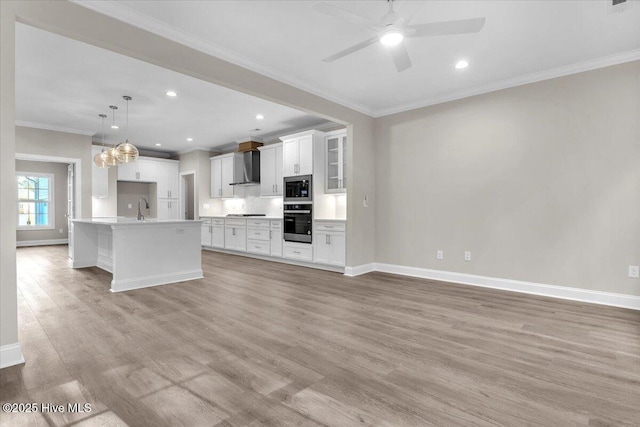 kitchen featuring stainless steel appliances, wall chimney range hood, light wood-type flooring, and a sink