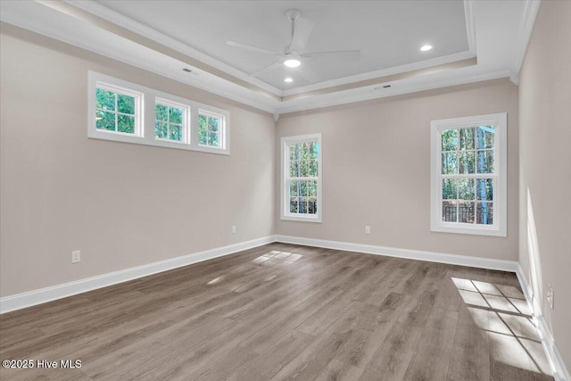 empty room featuring baseboards, ceiling fan, wood finished floors, a tray ceiling, and crown molding