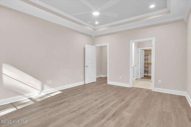 unfurnished bedroom featuring crown molding, a tray ceiling, baseboards, and light wood-style floors