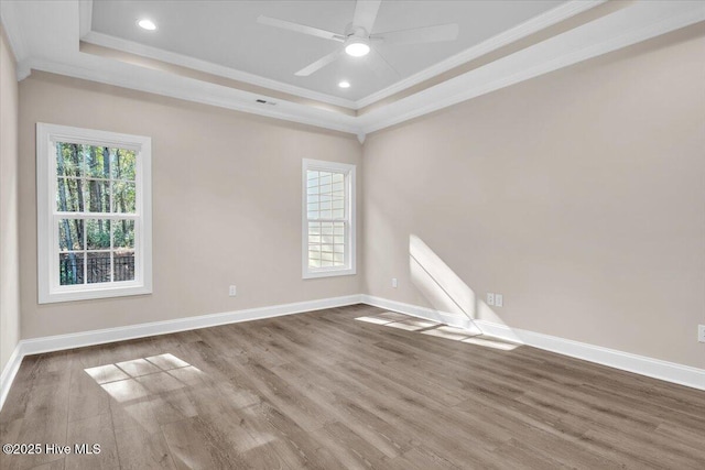 spare room with ornamental molding, a tray ceiling, baseboards, and wood finished floors