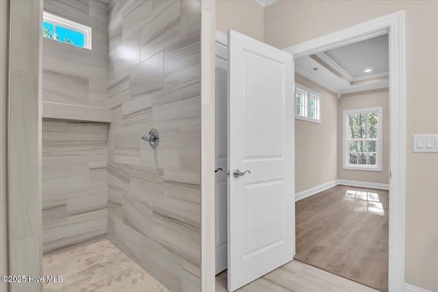 full bathroom featuring baseboards, a raised ceiling, wood finished floors, a tile shower, and crown molding