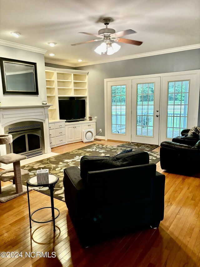 living room featuring built in shelves, crown molding, hardwood / wood-style floors, and ceiling fan