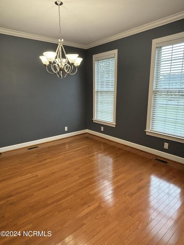 empty room featuring a chandelier, ornamental molding, visible vents, and wood finished floors