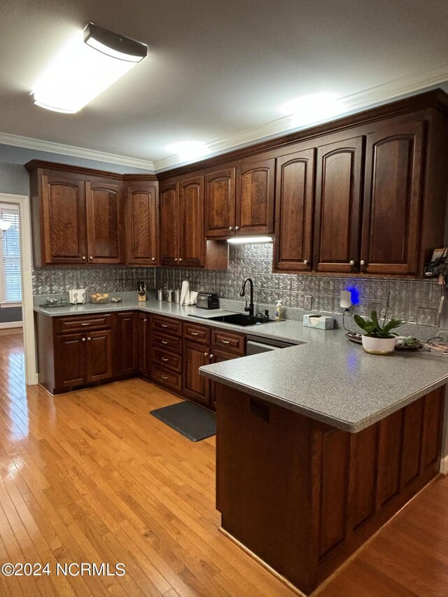 kitchen featuring kitchen peninsula, light hardwood / wood-style flooring, decorative backsplash, and ornamental molding