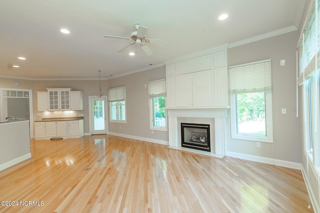 unfurnished living room featuring a large fireplace, ceiling fan, crown molding, and light wood-type flooring