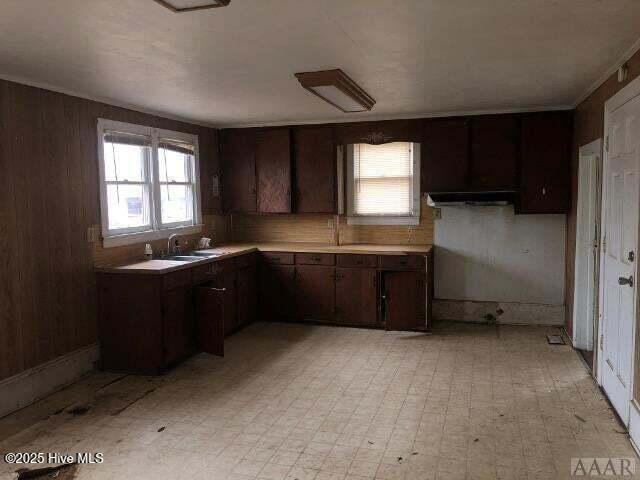 kitchen featuring a sink, dark brown cabinetry, wooden walls, light countertops, and light floors