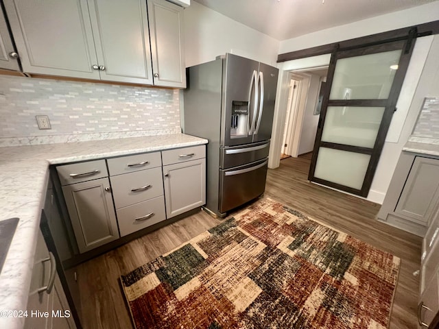 kitchen with a barn door, stainless steel fridge, light hardwood / wood-style flooring, and decorative backsplash