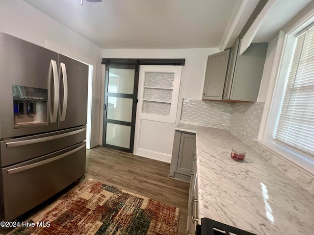 kitchen with a barn door, stainless steel refrigerator with ice dispenser, tasteful backsplash, and gray cabinets