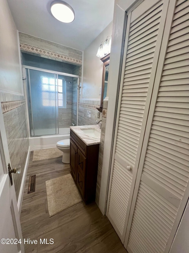 full bathroom with tile walls, vanity, hardwood / wood-style flooring, toilet, and combined bath / shower with glass door