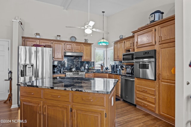 kitchen with a kitchen island, light hardwood / wood-style flooring, stainless steel appliances, dark stone counters, and ceiling fan