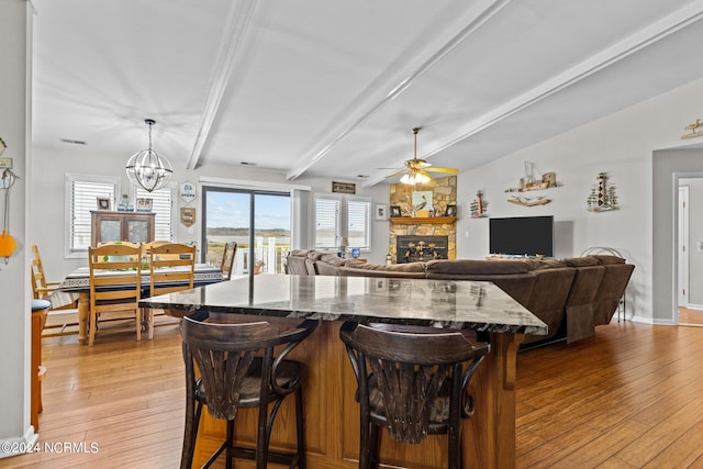 kitchen with dark stone countertops, a stone fireplace, light wood-type flooring, and ceiling fan with notable chandelier